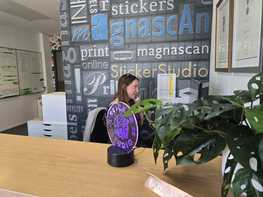 Camilla on the phone at the Sticker Studio front desk, with the glowing Sticker Studio sign behind