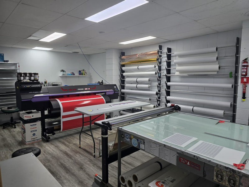 Mimaki UCJV printer room with racks of vinyl rolls and a cutting table