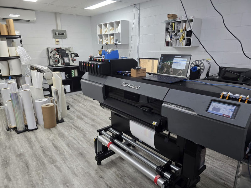 Roland TrueVIS wide-format printer with rolls of sticker material in the Sticker Studio workshop