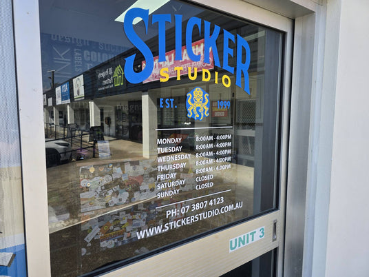 Sticker Studio shopfront window in Beenleigh showing the Est. 1999 logo, opening hours and phone number